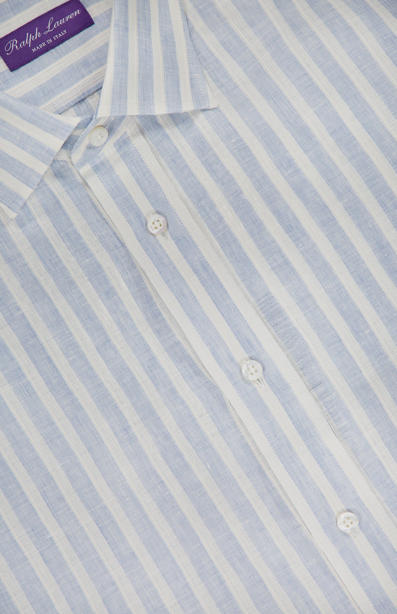 A close-up of the Linen Stripe Sport Shirt by RALPH LAUREN PURPLE LABEL, featuring light blue and white vertical stripes in lightweight, semi-sheer dobby linen, finished with elegant Mother of Pearl buttons.