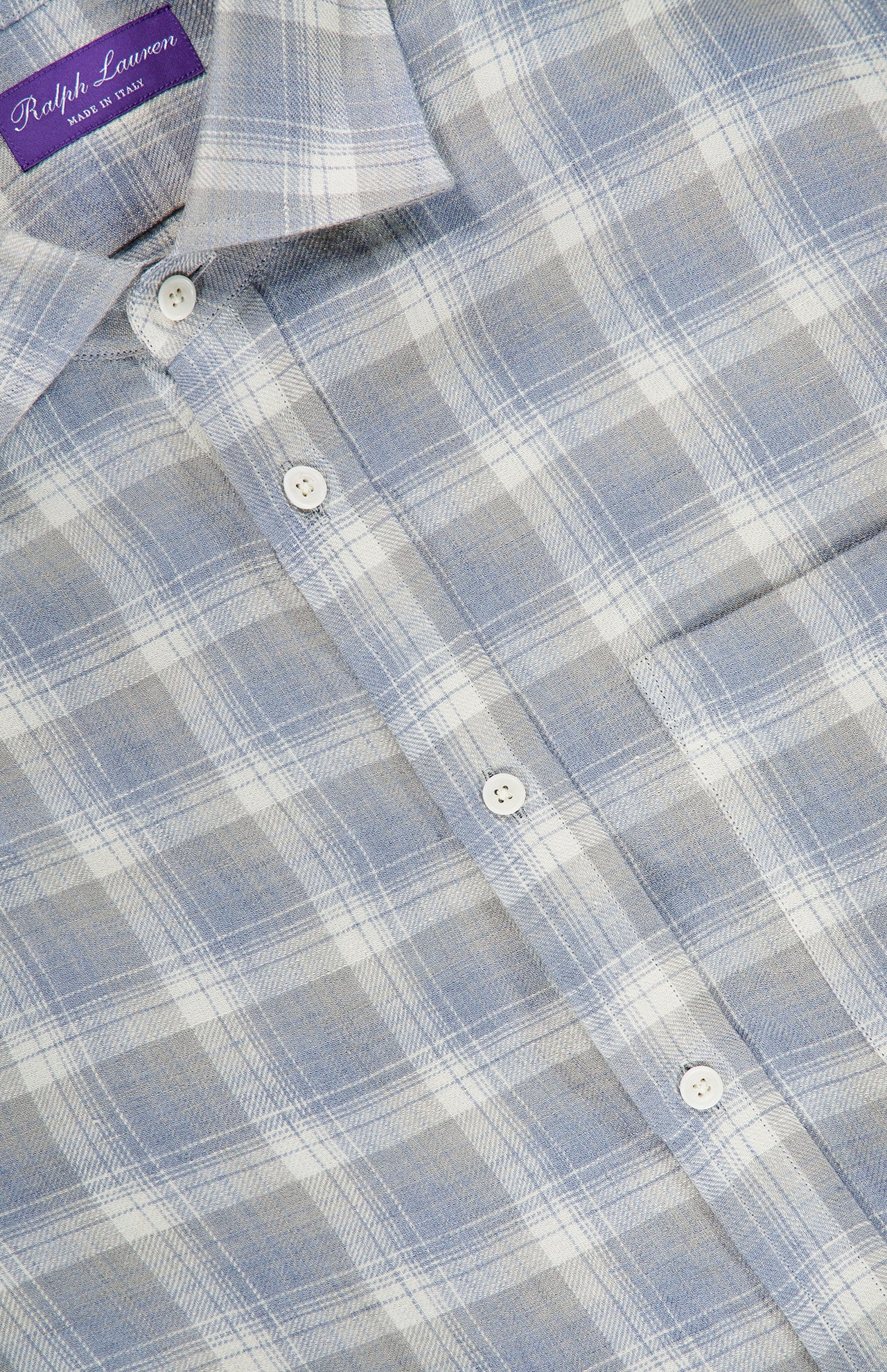 Close-up of a light blue, gray, and white plaid button-up shirt with a visible front pocket and collar. The label inside the collar reads RALPH LAUREN PURPLE LABEL. This Linen Twill Plaid Sport Shirt features pure linen construction, refined craftsmanship, and classic style—an ideal choice for those seeking a timeless men’s Italian shirt.