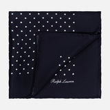 The RALPH LAUREN PURPLE LABEL Silk Foulard Dot Pocket Square is crafted in Italy in navy blue silk, featuring white polka dots in one corner and the Ralph Lauren logo embroidered in white on the opposite corner.