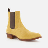 The Western Suede Mid Cut Boot by RALPH LAUREN PURPLE LABEL—a single yellow suede Chelsea boot featuring a brown elastic side panel, wooden heel, and pull tab—offers a modern interpretation of classic western style, shown against a white background.