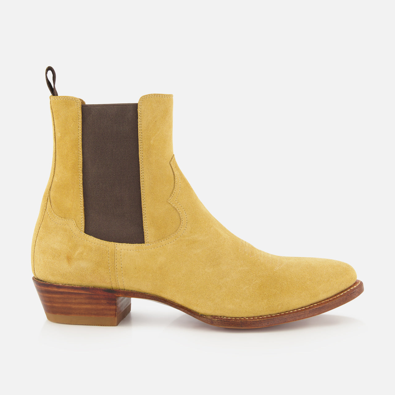 The RALPH LAUREN PURPLE LABEL Western Suede Mid Cut Boot, shown from the side on a white background, is a tan suede Chelsea-inspired design featuring classic western boot elements, including a brown elastic side panel, back pull tab, low stacked wooden heel, and brown sole.