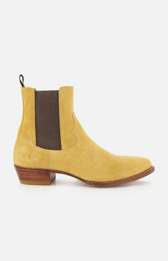 The RALPH LAUREN PURPLE LABEL Western Suede Mid Cut Boot, shown from the side on a white background, is a tan suede Chelsea-inspired design featuring classic western boot elements, including a brown elastic side panel, back pull tab, low stacked wooden heel, and brown sole.
