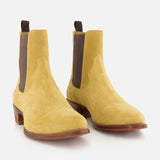 The RALPH LAUREN PURPLE LABEL Western Suede Mid Cut Boot is styled in the spirit of western boots, featuring yellow suede construction, brown elastic side panels, and wooden soles, positioned on a white background.