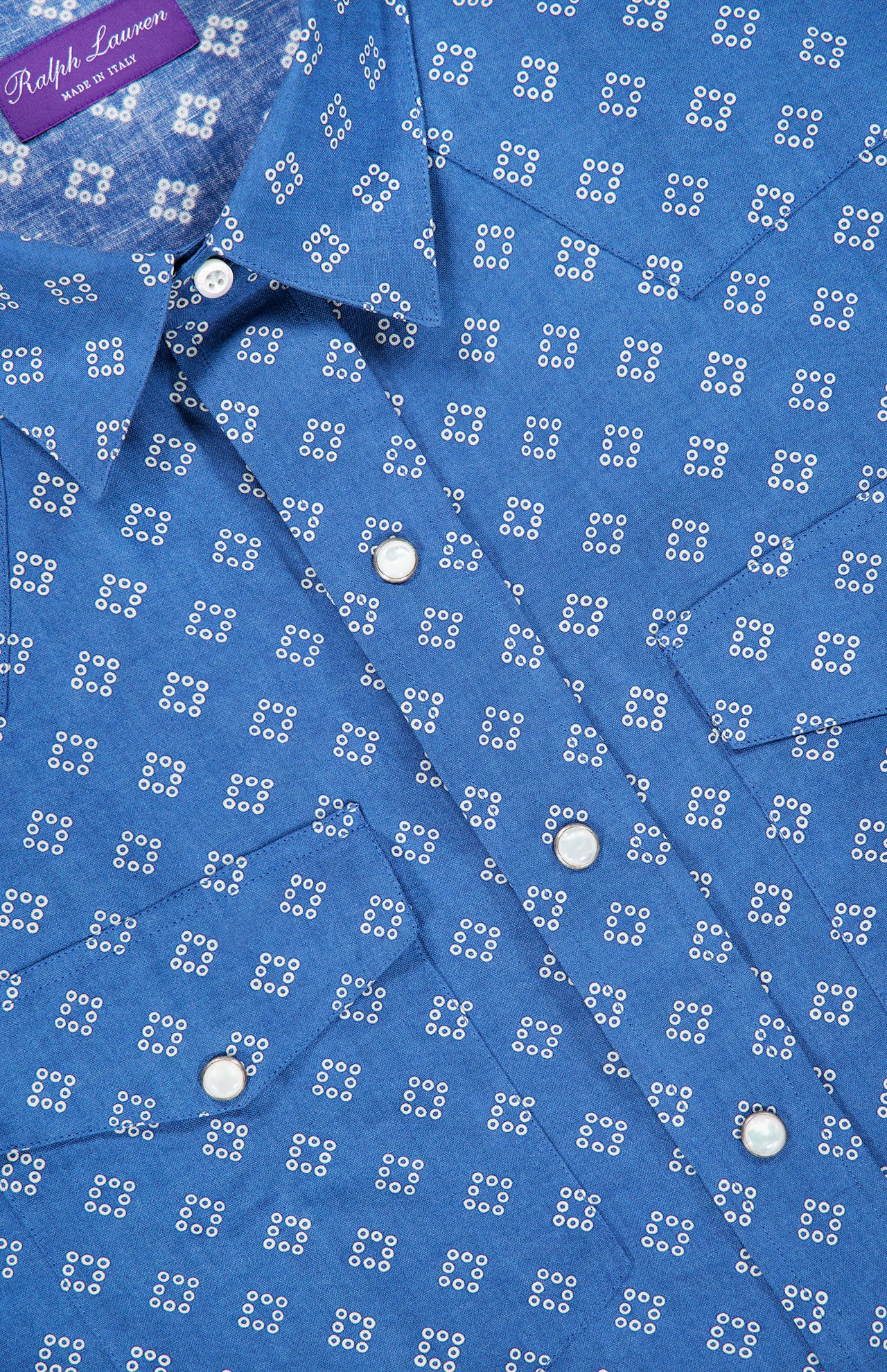A close-up of the RALPH LAUREN PURPLE LABEL Western Wendover Bandana Sport Shirt, showcasing its rich blue hue reminiscent of indigo, adorned with a crisp white geometric square pattern and accented by white buttons.