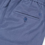 Close-up of the Silk Linen Dorset Flat Front Trouser by Ralph Lauren Purple Label, featuring blue silk-linen fabric, an elastic waistband, a buttoned back pocket, and an embroidered R logo.