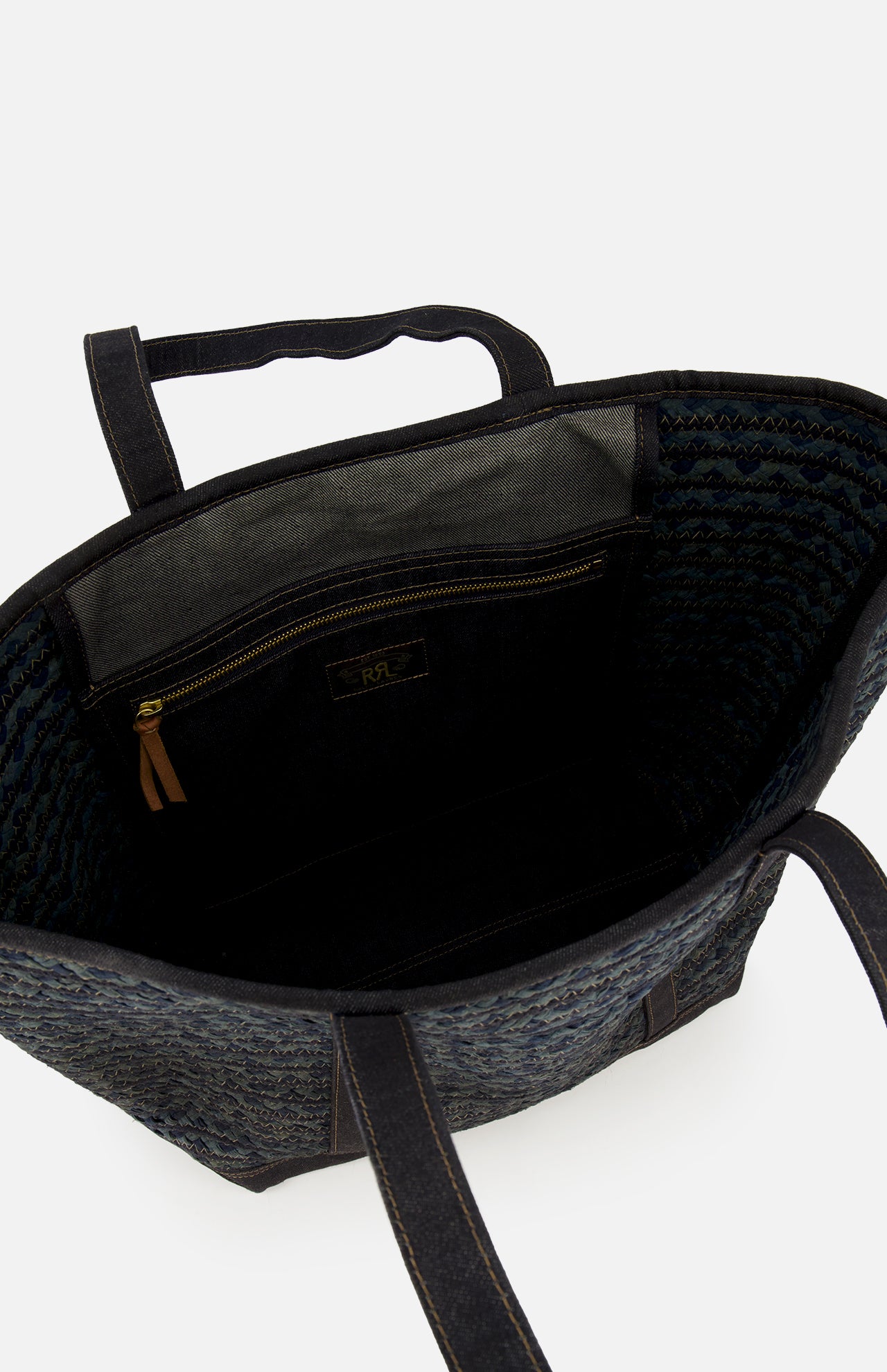 Open top view of the Cotton Banks Beach Bag by RALPH LAUREN RRL, hand braided in navy and black with indigo denim handles, showing its interior zippered pocket and small label. Features a textured dark blue pattern.
