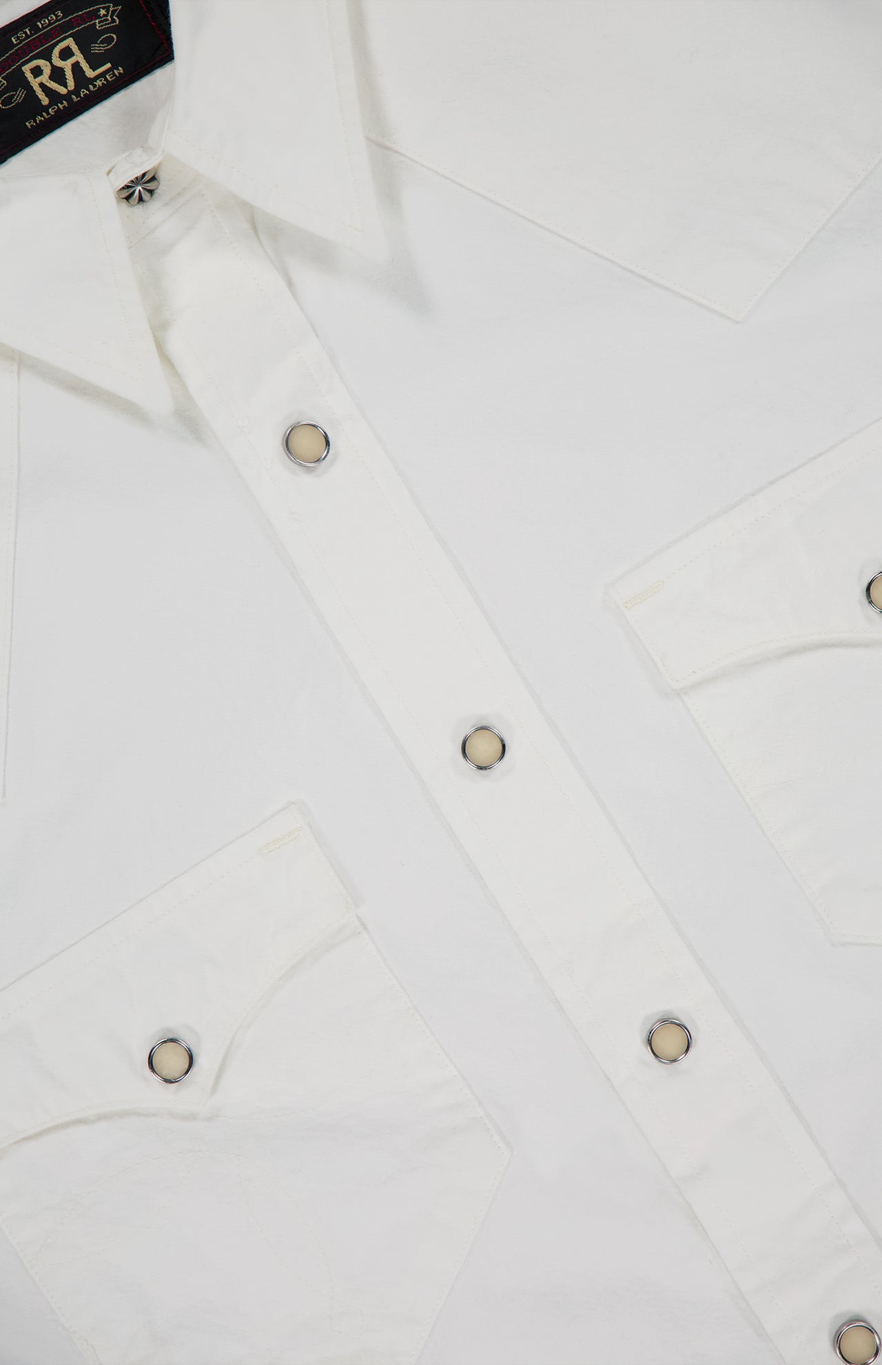 Close-up of the RALPH LAUREN RRL Cotton Poplin Buffalo Western Workshirt, showcasing white cotton poplin fabric, two front chest pockets, metal snap buttons, and a visible shirt collar with part of the inner label—classic Western details.