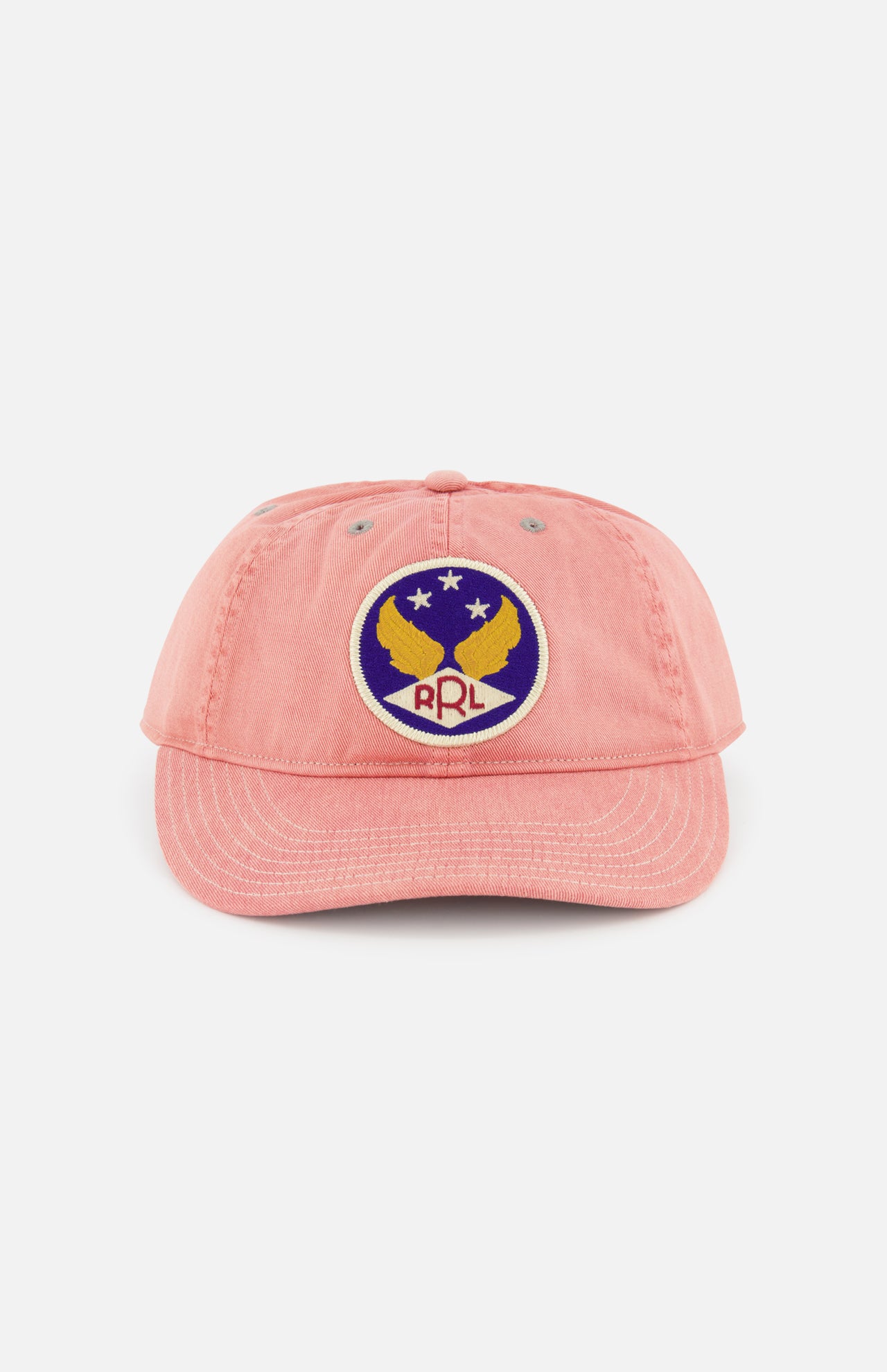 The Cotton Twill Faded Ball Hat by RALPH LAUREN RRL features soft pink cotton twill, a curved brim, and an embroidered patch with two yellow eagles, a star, and “RRL” on a blue and white circular background for vintage style.