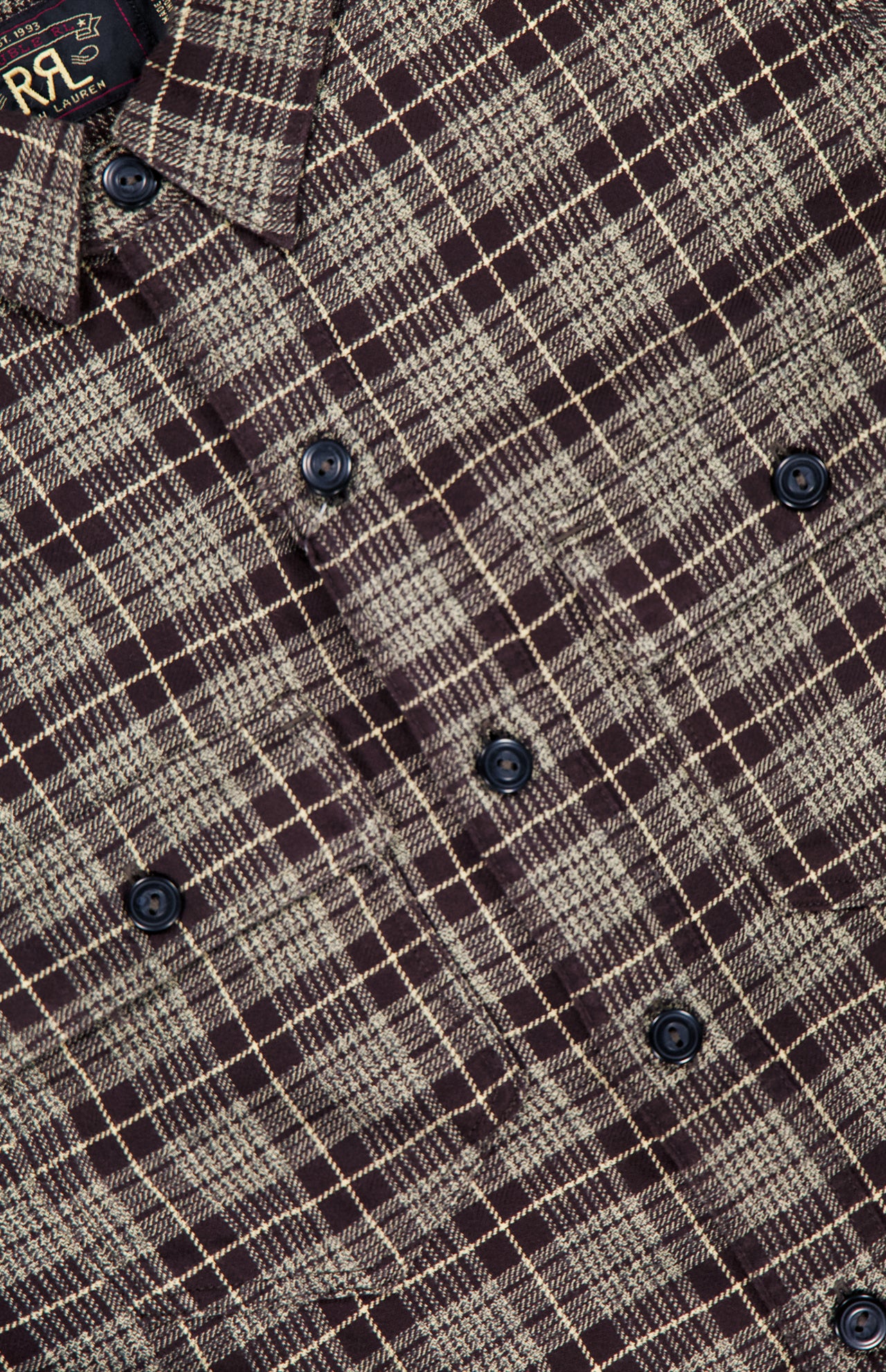 Close-up of the Eaton Cotton Sport Shirt by RALPH LAUREN RRL, featuring a brown and beige plaid cotton twill fabric with black buttons. The checkered pattern evokes a vintage workshirt style, and a clothing tag with the RRL logo is partially visible at the top left corner.