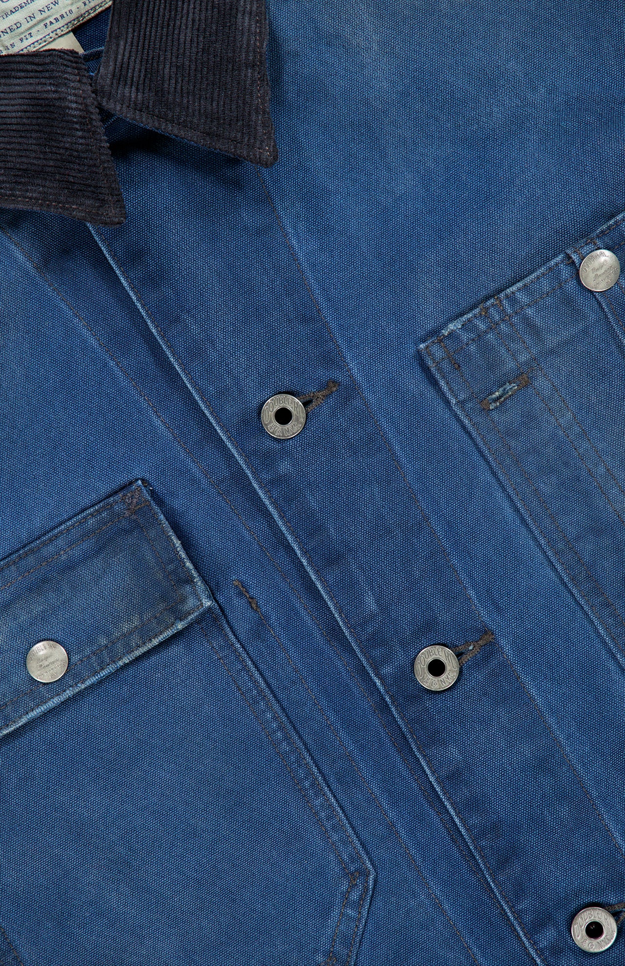 Close-up of the Ellis Cotton Long Sleeve Work Shirt by RALPH LAUREN RRL, featuring blue denim fabric, silver buttons, two chest pockets with visible stitching, and a dark corduroy collar. The texture of the fabric and the details of the pockets and collar are clearly shown.