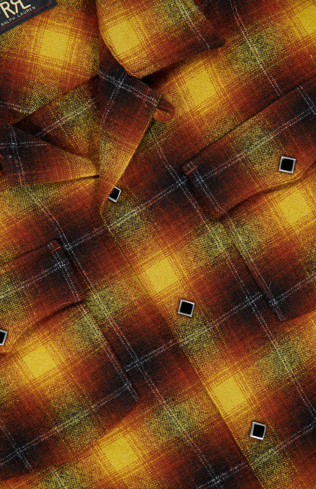A close-up of the Jesse Plaid Cotton Camp Shirt by RALPH LAUREN RRL, featuring a yellow, orange, and brown plaid pattern with black and white buttons, highlighting its detailed texture and stitching.