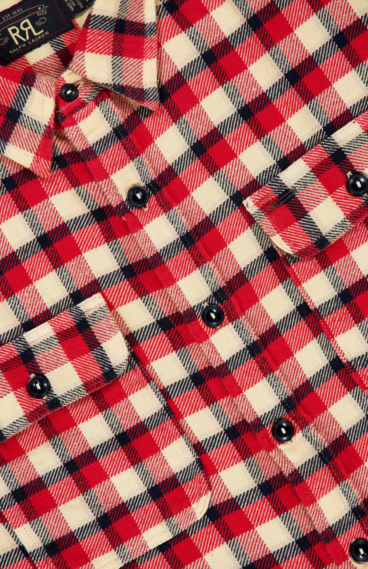 Close-up of the Matlock Plaid Cotton Sport Shirt by RALPH LAUREN RRL, featuring a red, white, and black plaid pattern with black buttons and two chest pockets. Designed in the style of a vintage workshirt, this shirt showcases a partially visible label in the top left corner.