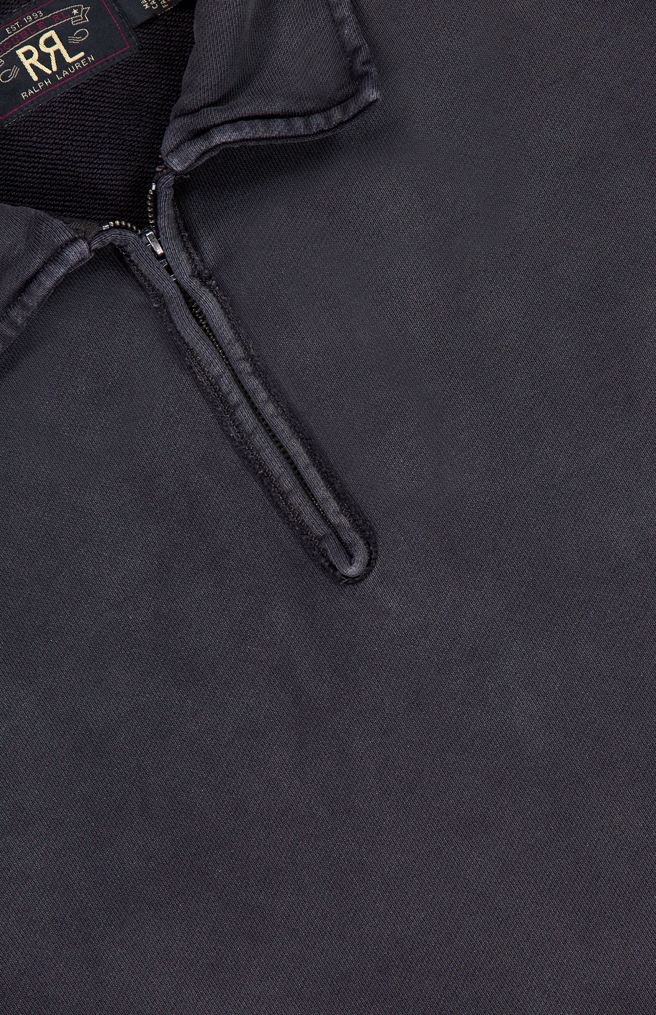Close-up of the Terry Quarter Zip Pullover Sweatshirt from RALPH LAUREN RRL in dark gray, featuring a smooth yet slightly textured fabric. The shirt’s collar showcases a short zipper that is partially open, evoking the timeless look of a classic quarter zip style. Inside the collar, you'll find an RR and Ralph Lauren label—making this pullover an ideal choice for stylish comfort during travel.