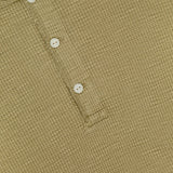 Close-up of the RALPH LAUREN RRL Waffle Knit Long Sleeve Henley Shirt, showcasing its beige textured waffle-knit fabric and three vintage-inspired buttons on a short placket. The shirt is laid flat to emphasize the intricate pattern and precise stitching details.