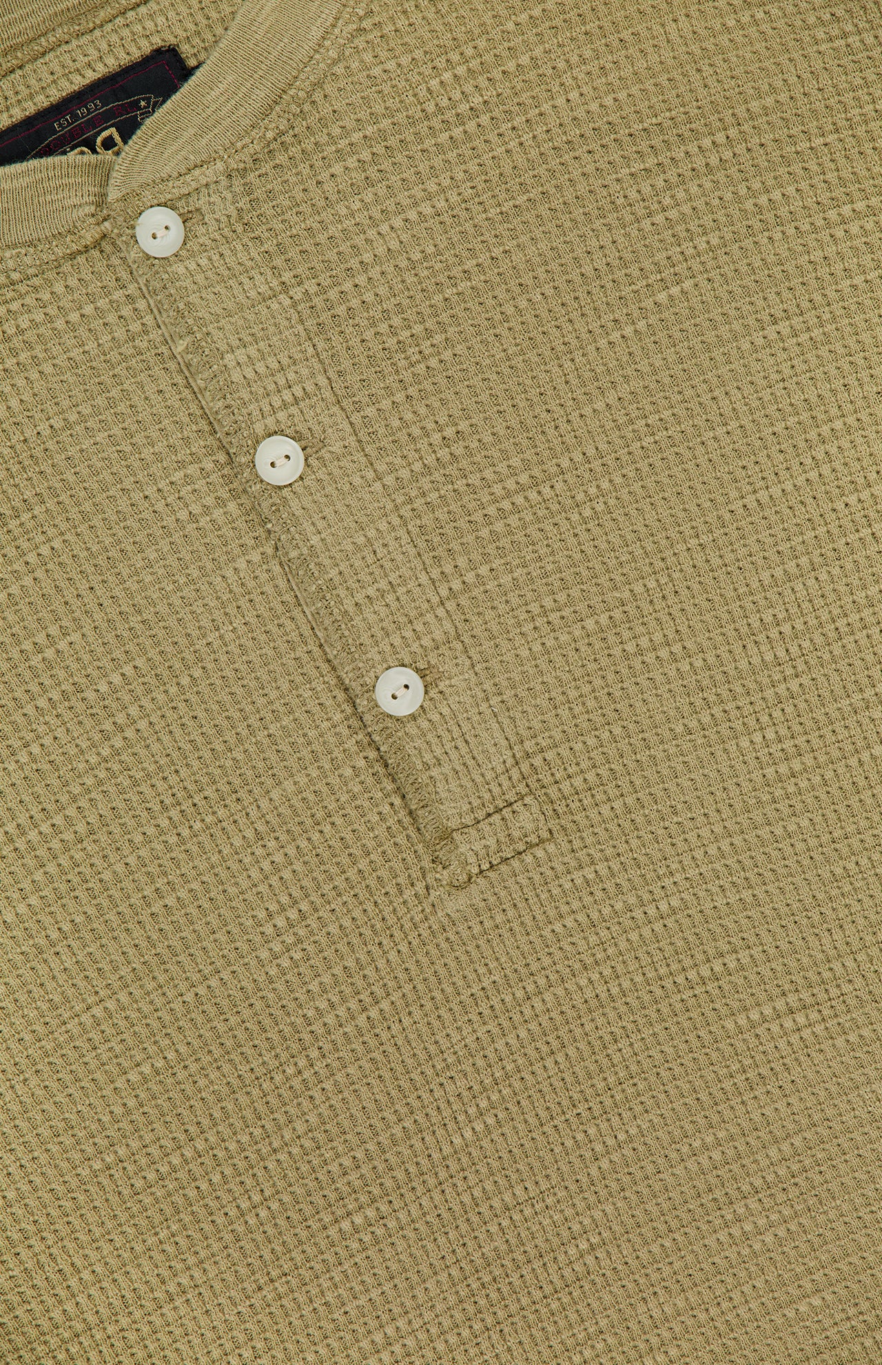 Close-up of the RALPH LAUREN RRL Waffle Knit Long Sleeve Henley Shirt, showcasing its beige textured waffle-knit fabric and three vintage-inspired buttons on a short placket. The shirt is laid flat to emphasize the intricate pattern and precise stitching details.