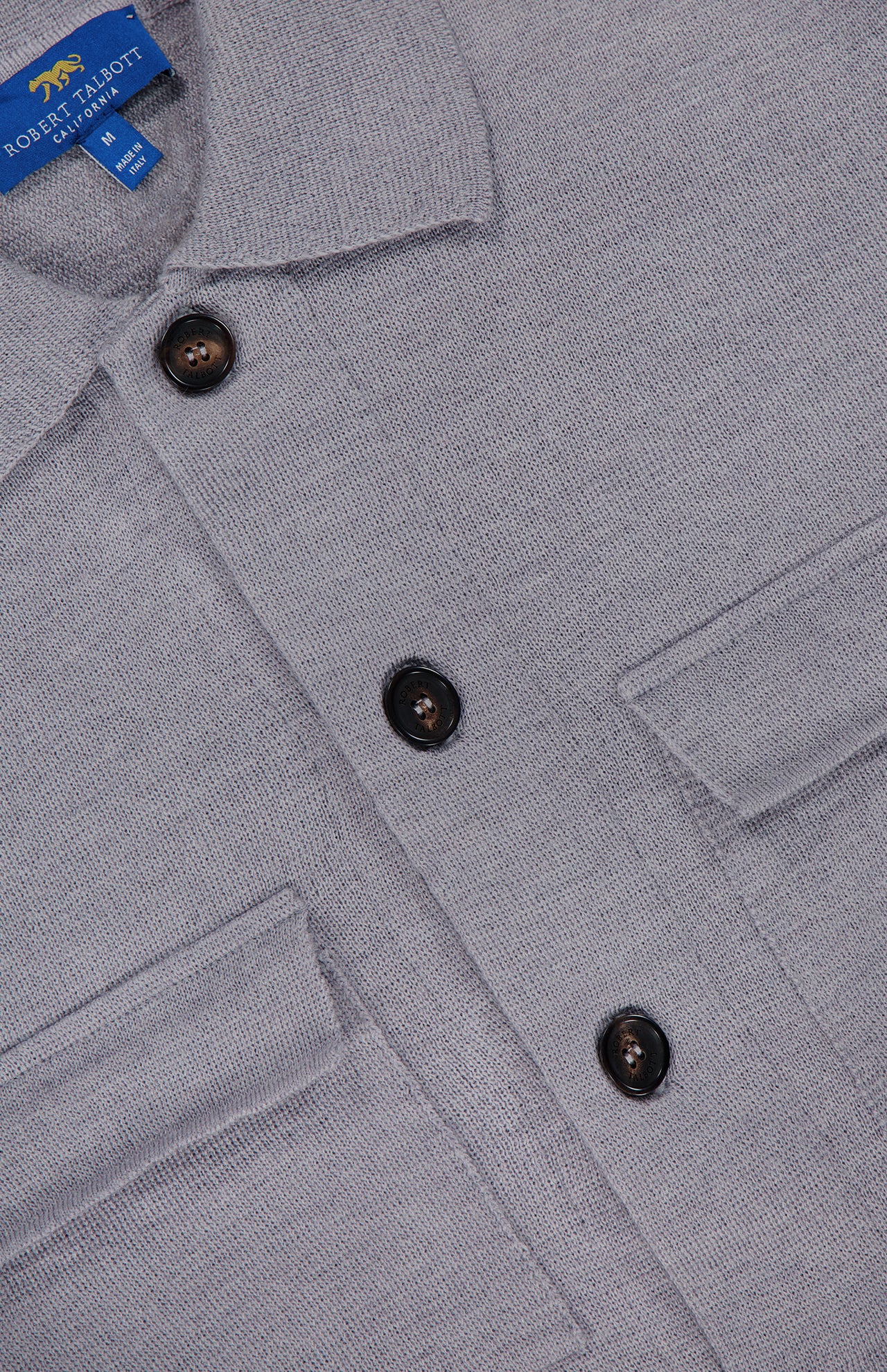 Close-up of the Landon Sweater Jacket, a light gray button-up by ROBERT TALBOTT featuring two chest pockets and dark buttons. The inside collar label displays ROBERT TALBOTT TAILORED FIT. Designed in a tailored fit, this piece combines the polished look of a classic shirt with the versatility of a hybrid sweater-jacket, making it perfect for layering throughout any season.