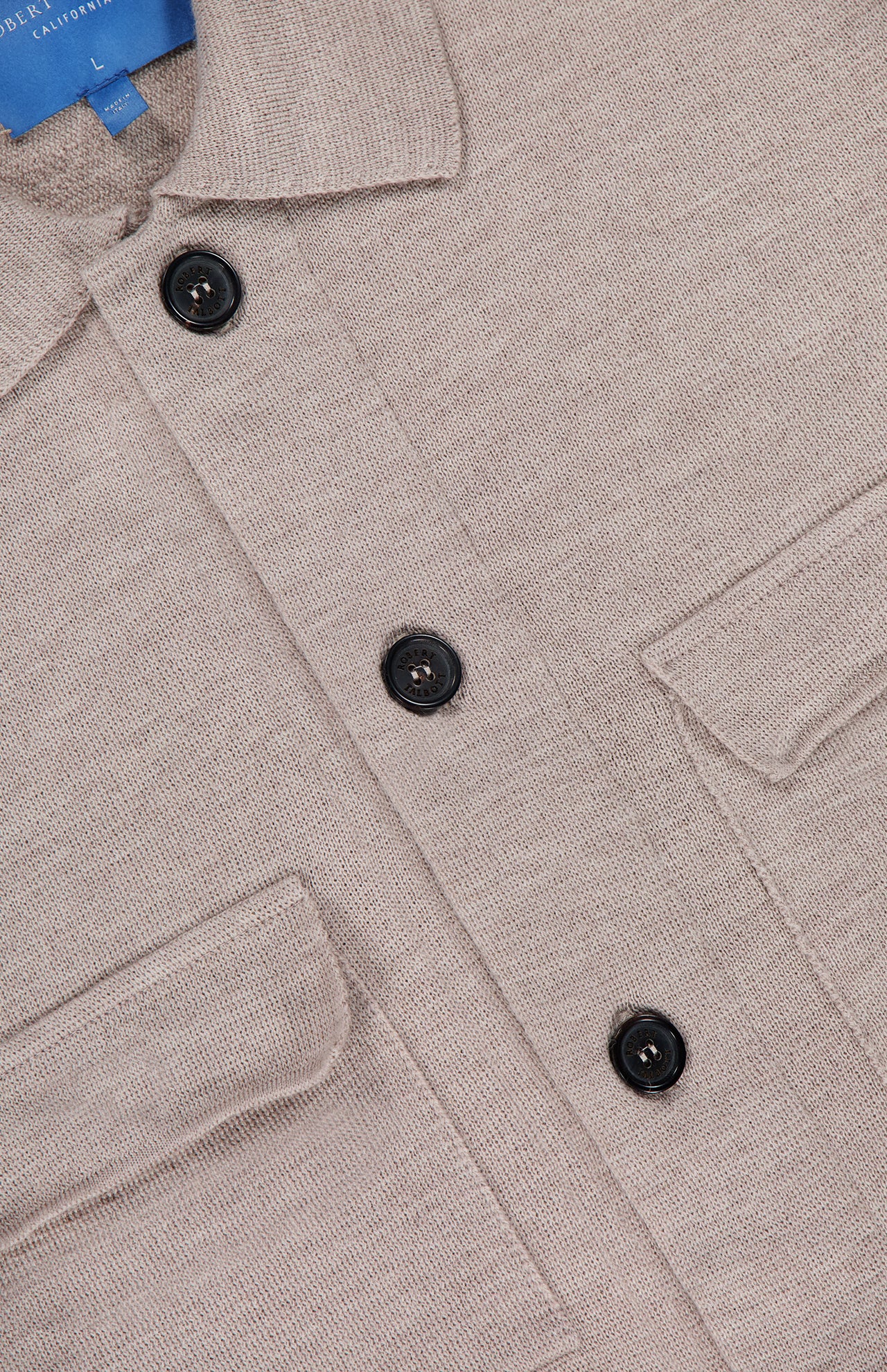 Close-up of the ROBERT TALBOTT Landon Sweater Jacket in beige, showcasing its tailored fit, textured fabric, black buttons, two chest pockets, and a partially visible blue tag at the collar.