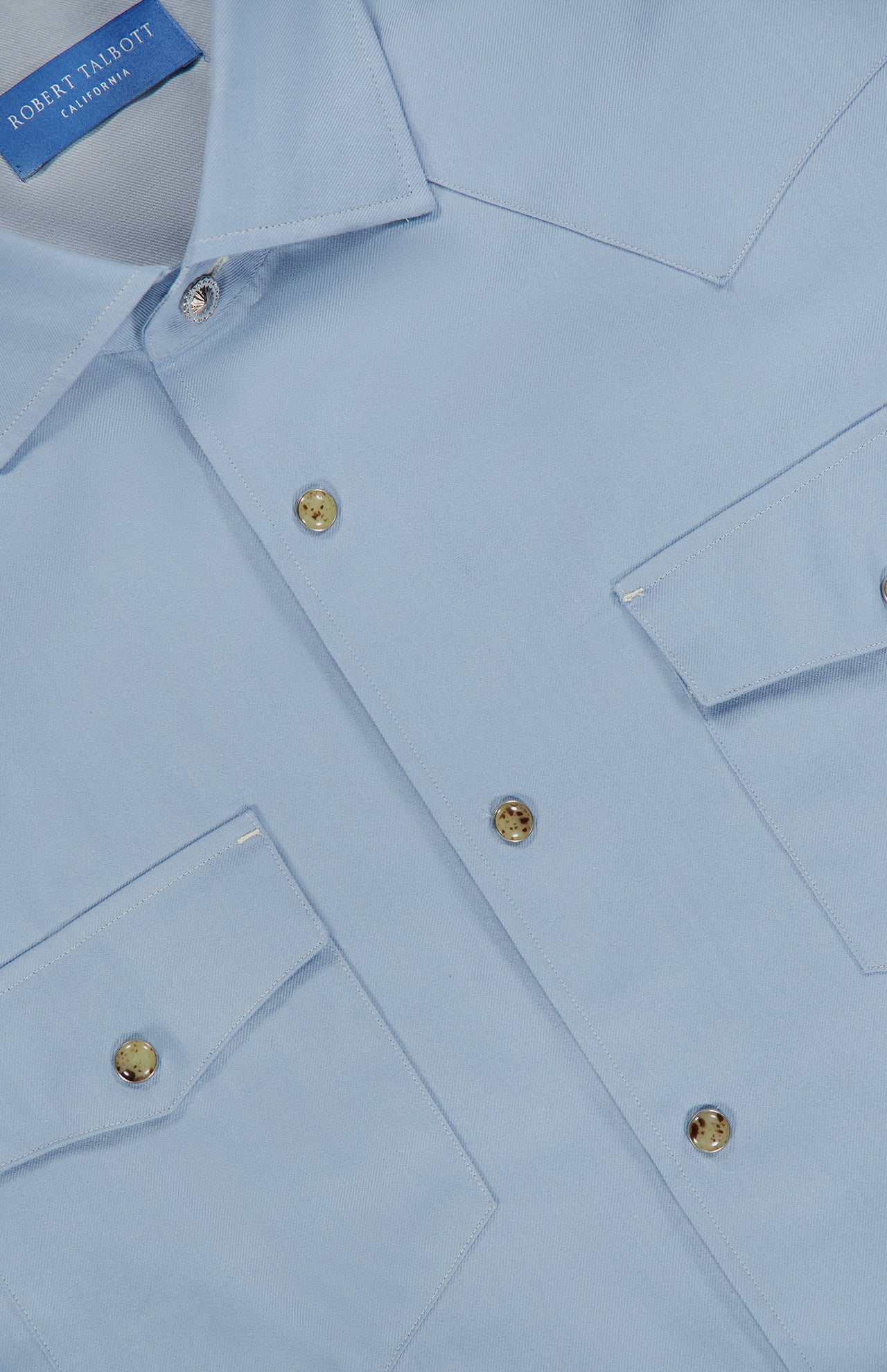 Close-up of a light blue McQueen Western Cashmere Twill Shirt by ROBERT TALBOTT, featuring two front pockets, gold-tone buttons, and a visible blue label inside the collar.