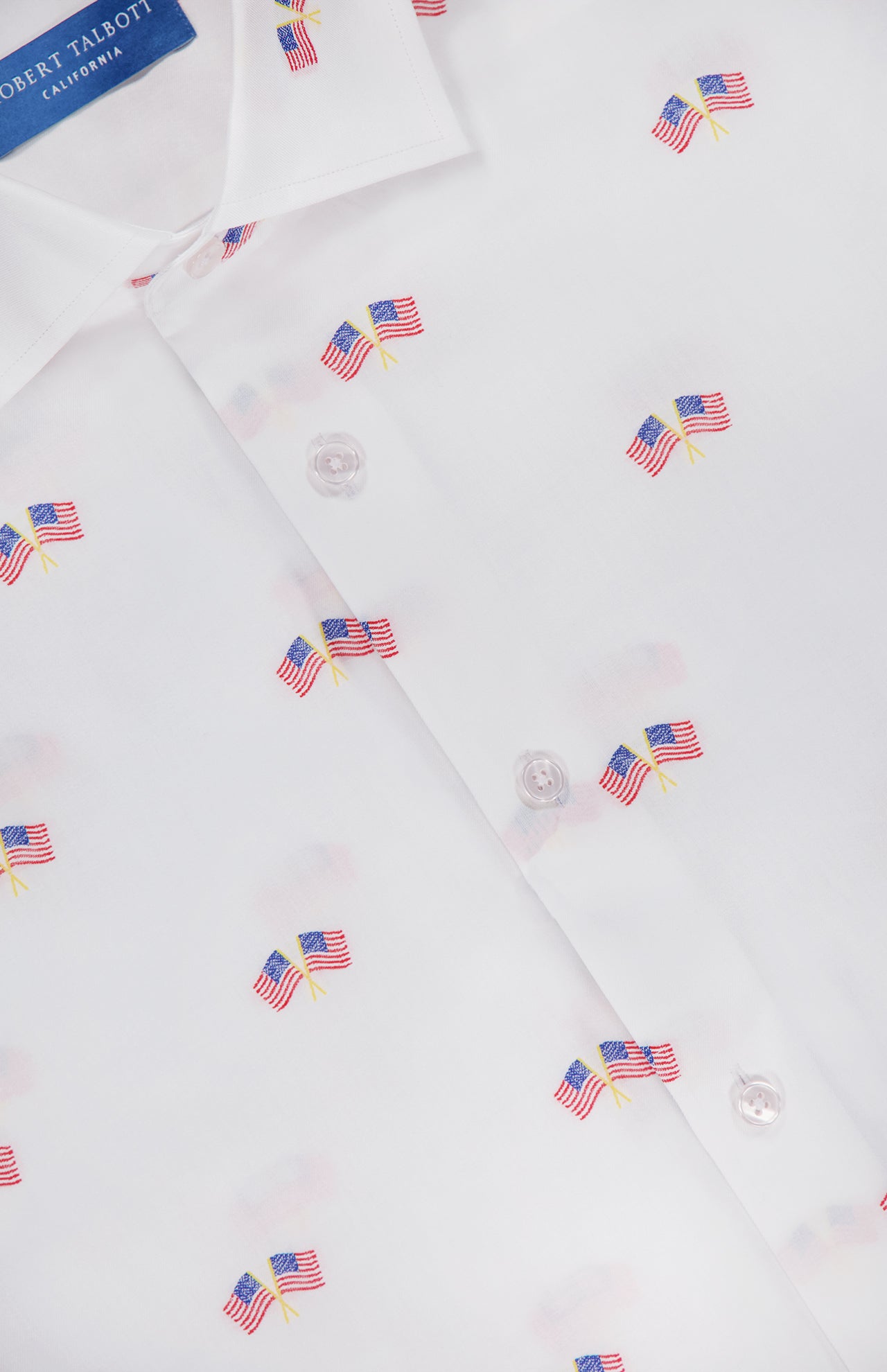 Close-up of the Reynolds Flag Coupe Twill Dress Shirt by ROBERT TALBOTT, a white sport shirt with a small American flag print and a collar showcasing the blue Robert Talbott California label. Ideal for everyday wear.