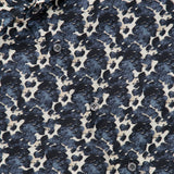 Close-up of the Reynolds Printed Cow Hide Dress Shirt by ROBERT TALBOTT, showcasing a distinctive cowhide pattern in dark blue and white on dark navy fabric, with black buttons and a partially visible ROBERT TALBOTT label in the top left corner. Expertly crafted from an Italian silk cotton-blend, this shirt delivers both elegance and comfort.