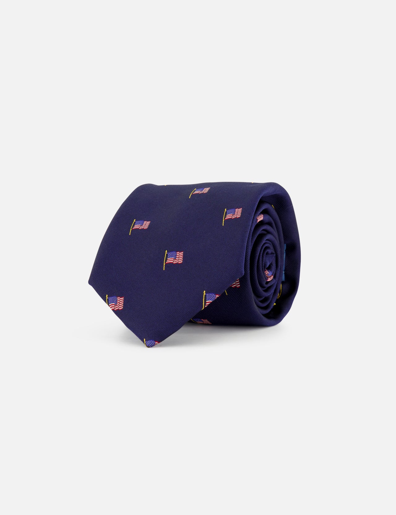 The Robert American Flag Neck Tie by ROBERT TALBOTT is a rolled-up silk navy tie with a repeating American flag print on a plain light gray background.
