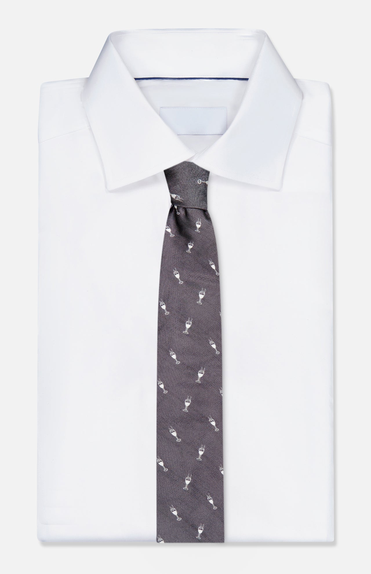 A neatly folded white dress shirt with the ROBERT TALBOTT Robert Champagne Glass Tie—a dark grey silk tie featuring a repeating champagne glass pattern.