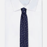 A neatly folded white dress shirt with a wide collar, paired with the ROBERT TALBOTT Robert Dollar Signs Tie—a classic navy silk tie adorned with a subtle white polka dot pattern—displayed against a plain white background.