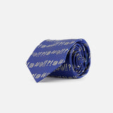 The Robert Grawlix Tie by ROBERT TALBOTT is a luxury blue silk necktie, rolled up and adorned with a repeating grawlix print of white exclamation points, question marks, and spirals, all showcased on a plain white background.