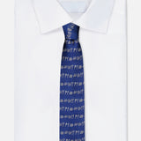 A folded white dress shirt is paired with the ROBERT TALBOTT Robert Grawlix Tie—a luxurious blue silk necktie showcasing a playful grawlix print of repeated white symbols (@, #, !, ?), evoking comic-style exclamations.