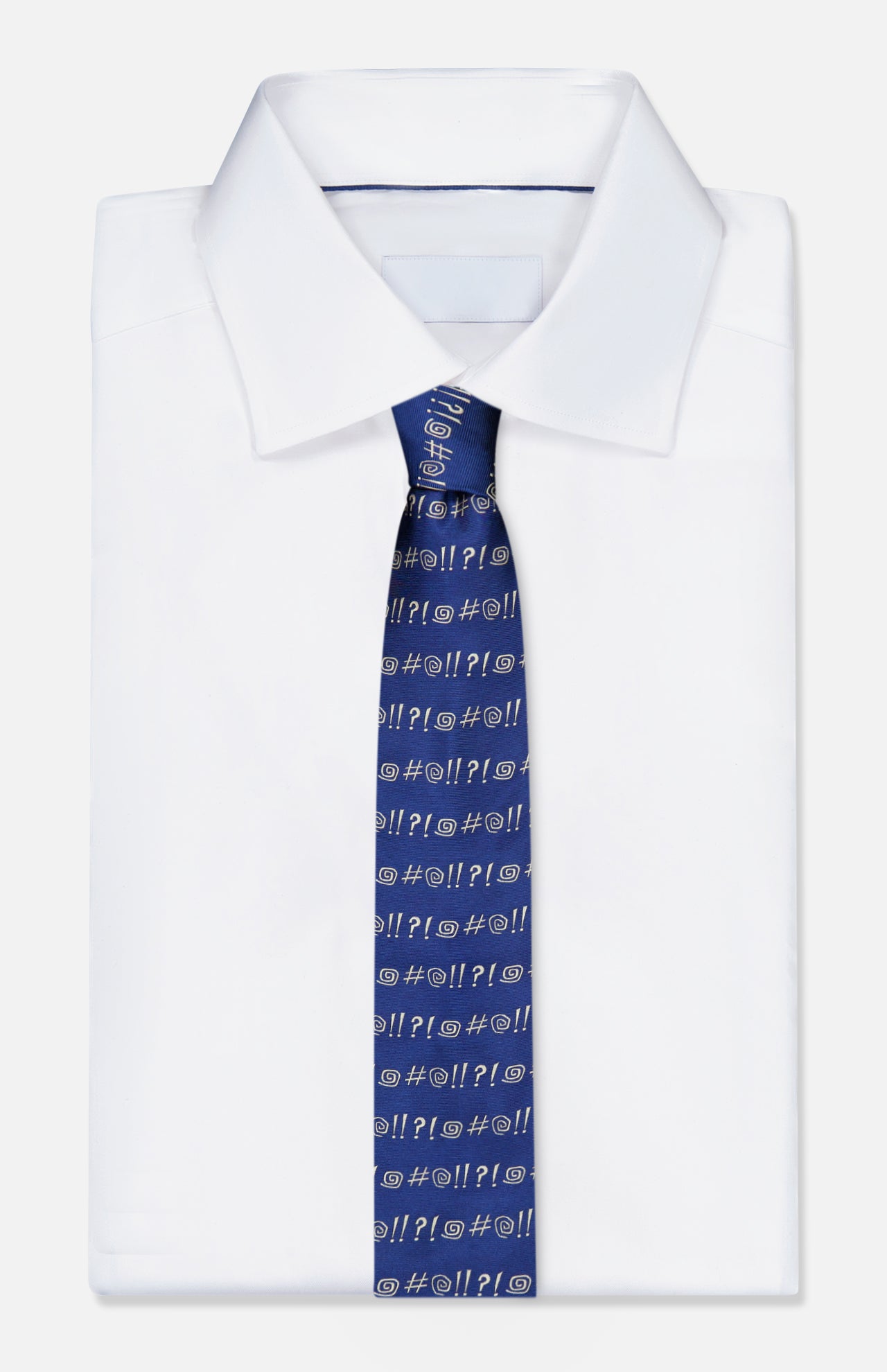 A folded white dress shirt is paired with the ROBERT TALBOTT Robert Grawlix Tie—a luxurious blue silk necktie showcasing a playful grawlix print of repeated white symbols (@, #, !, ?), evoking comic-style exclamations.