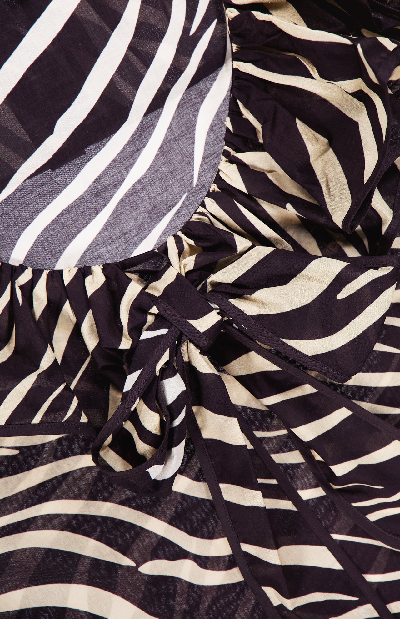 Close-up of the Aubrey Zebra Print Ruffle Top by RONNY KOBO, featuring black and white animal stripes, ruffled edges, and a tied bow detail.