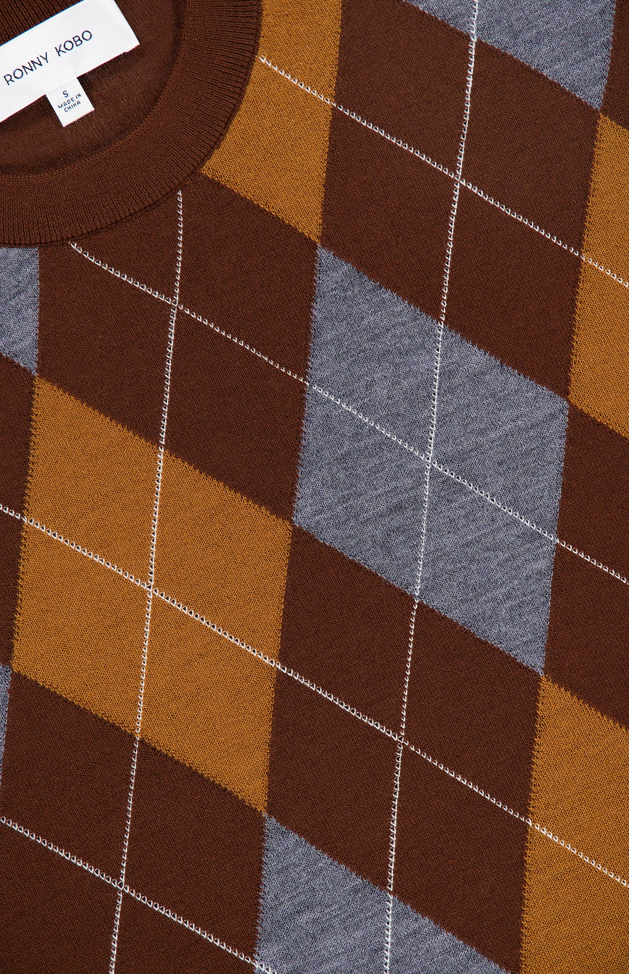Close-up of the Bradley Argyle Sweater by RONNY KOBO, showcasing its wool cashmere blend and distinctive brown, mustard, and gray argyle pattern with visible white stitching. The brand’s tag appears in the top left corner.
