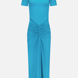The RONNY KOBO Enid Ruched Detail Maxi Dress is a vibrant turquoise gown with short sleeves, a high neckline, ruched waist, and elegant draped folds flowing down its maxi-length skirt—perfect for wedding guests.
