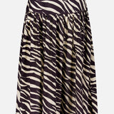 The Feyre Animal Print Skirt by RONNY KOBO is a knee-length, flared design with a high waist and bold black-and-white zebra print. It features gathered fabric at the waistband for a full, flowing silhouette and has a subtle sheen.