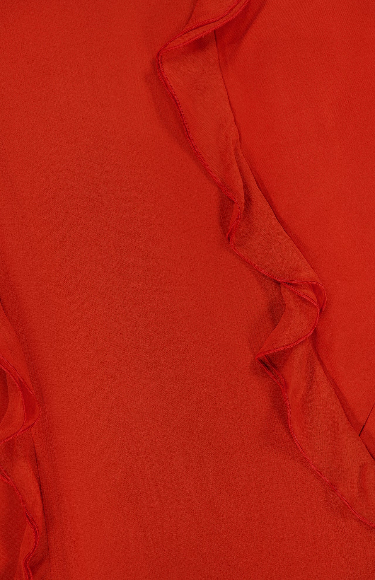 Close-up of the Milena Draping Maxi Dress by RONNY KOBO, showcasing red fabric with wavy, ruffled edges that run diagonally across the image, creating a textured and layered look evocative of fluid draping.
