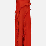 The Milena Draping Maxi Dress by RONNY KOBO is a sleeveless, vibrant red dress with thin spaghetti straps, showcasing fluid draping and a ruffled detail that cascades diagonally from the waist to the hem. It features a subtle thigh-high slit for an added touch of elegance.