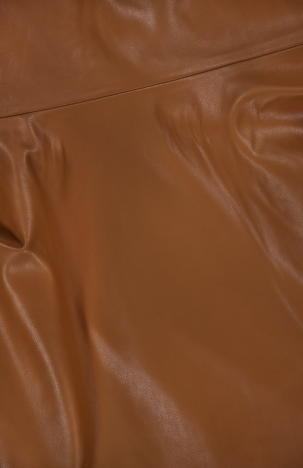 Close-up of the Pelle Faux Leather Mini Dress by RONNY KOBO, featuring smooth, dark brown faux leather fabric with gentle folds and subtle creases that reflect light, highlighting its texture and sheen.