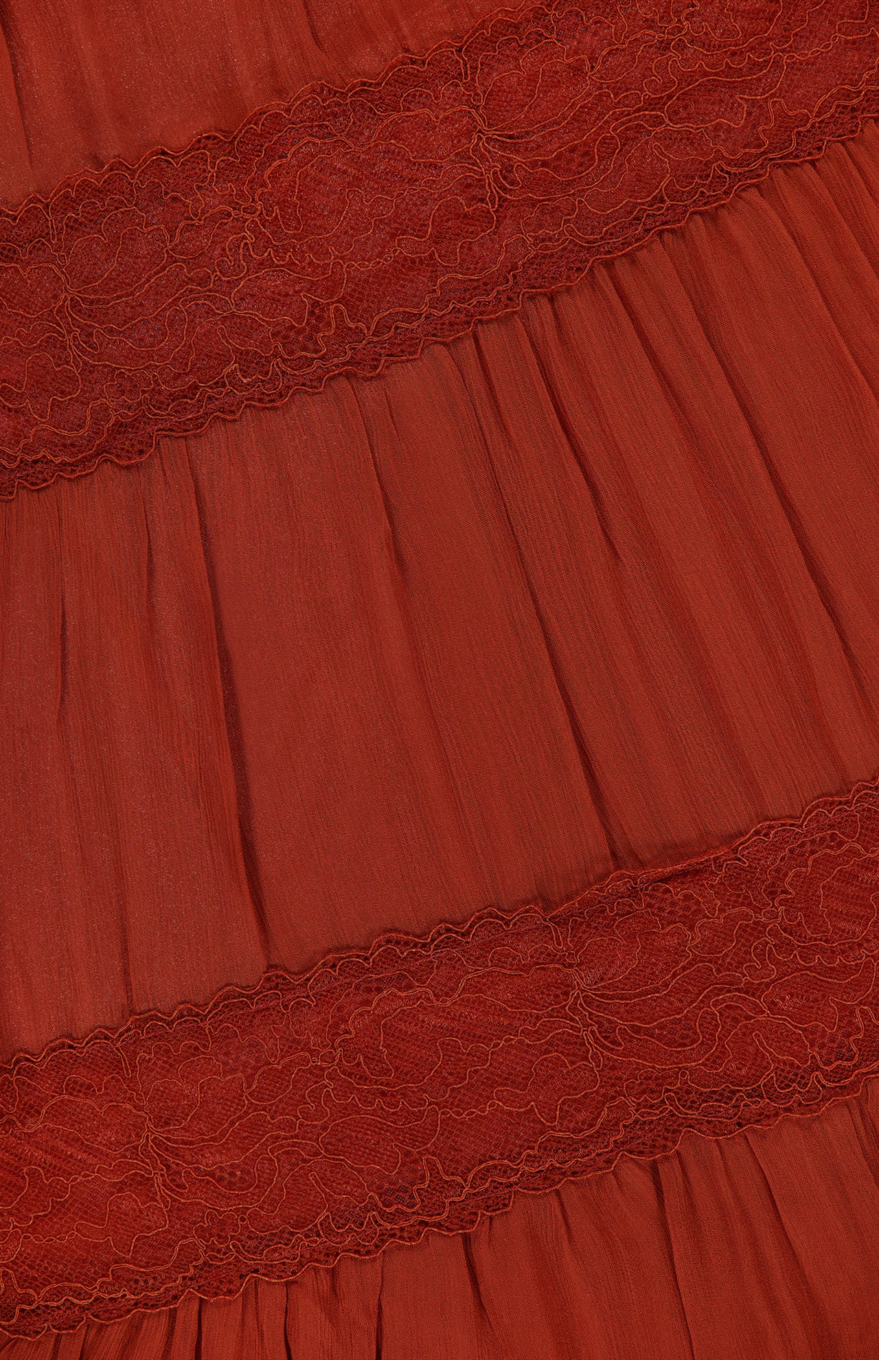 Close-up of the RONNY KOBO Rune Lace Panel Maxi Dress in rust, showcasing pleated fabric and horizontal lace panels for a textured, layered look inspired by bohemian style.
