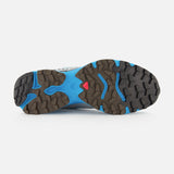 The image shows the bottom of a blue and brown SALOMON XT-4 OG Sneaker, featuring a rugged, textured outsole engineered for stability and grip, with a small red triangular detail near the center—distinctive elements of this performance footwear designed for traction.