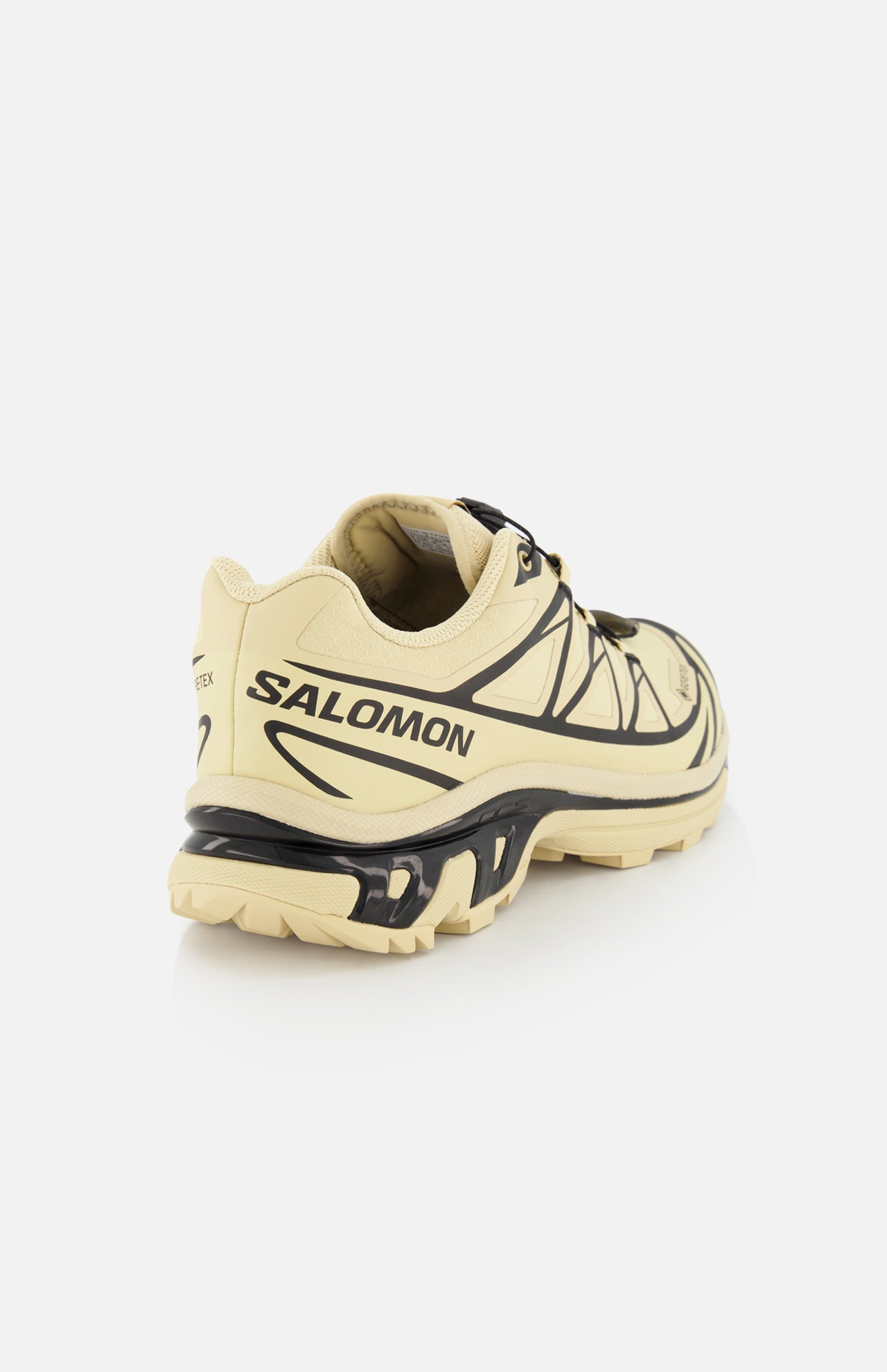 The SALOMON XT-6 GTX Sneaker, shown from the back left, is a beige trail shoe with black accents, "SALOMON" branding on the heel, a rugged sole, and a quick lace system for easy adjustment on any trail.