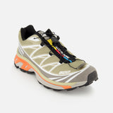 Salomon XT-6 sneaker in olive green with a quick-lace system, white geometric overlays, and a cushioned orange midsole.