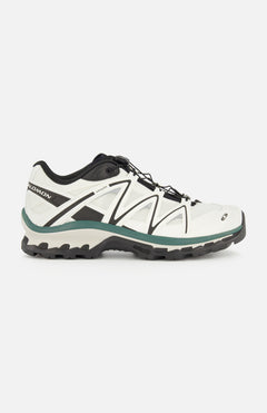 Side view of the SALOMON XT-Quest Sneaker in white and black, featuring a rugged black sole, green-gray accents, and lace-up closure; this hybrid performance sneaker is designed to blend urban wearability with enhanced stability and grip, shown against a plain white background.