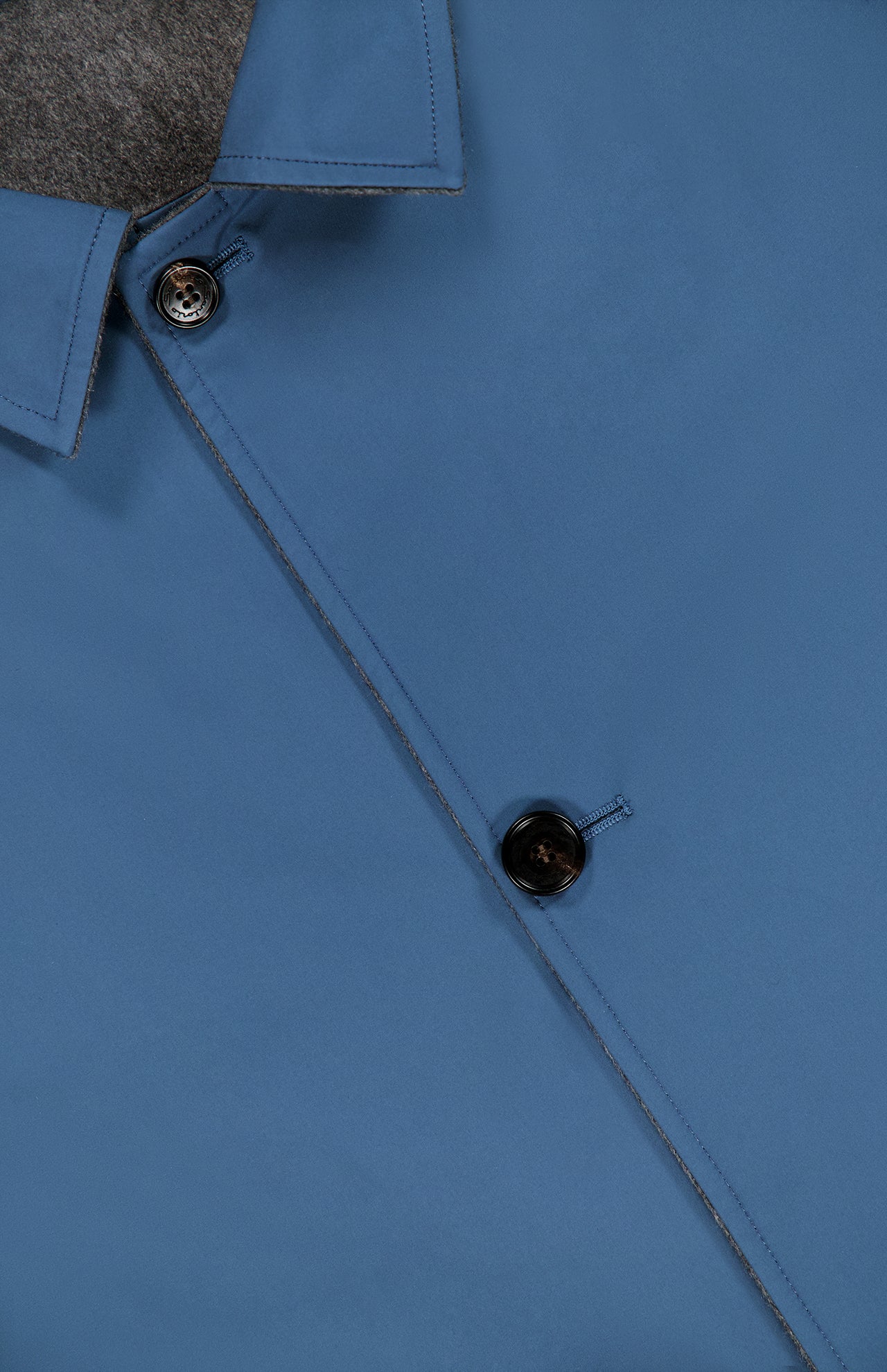 Close-up of a blue button-up shirt with two black buttons visible and gray inner lining near the collar, styled underneath the SARTORIO Double Faced Overcoat.