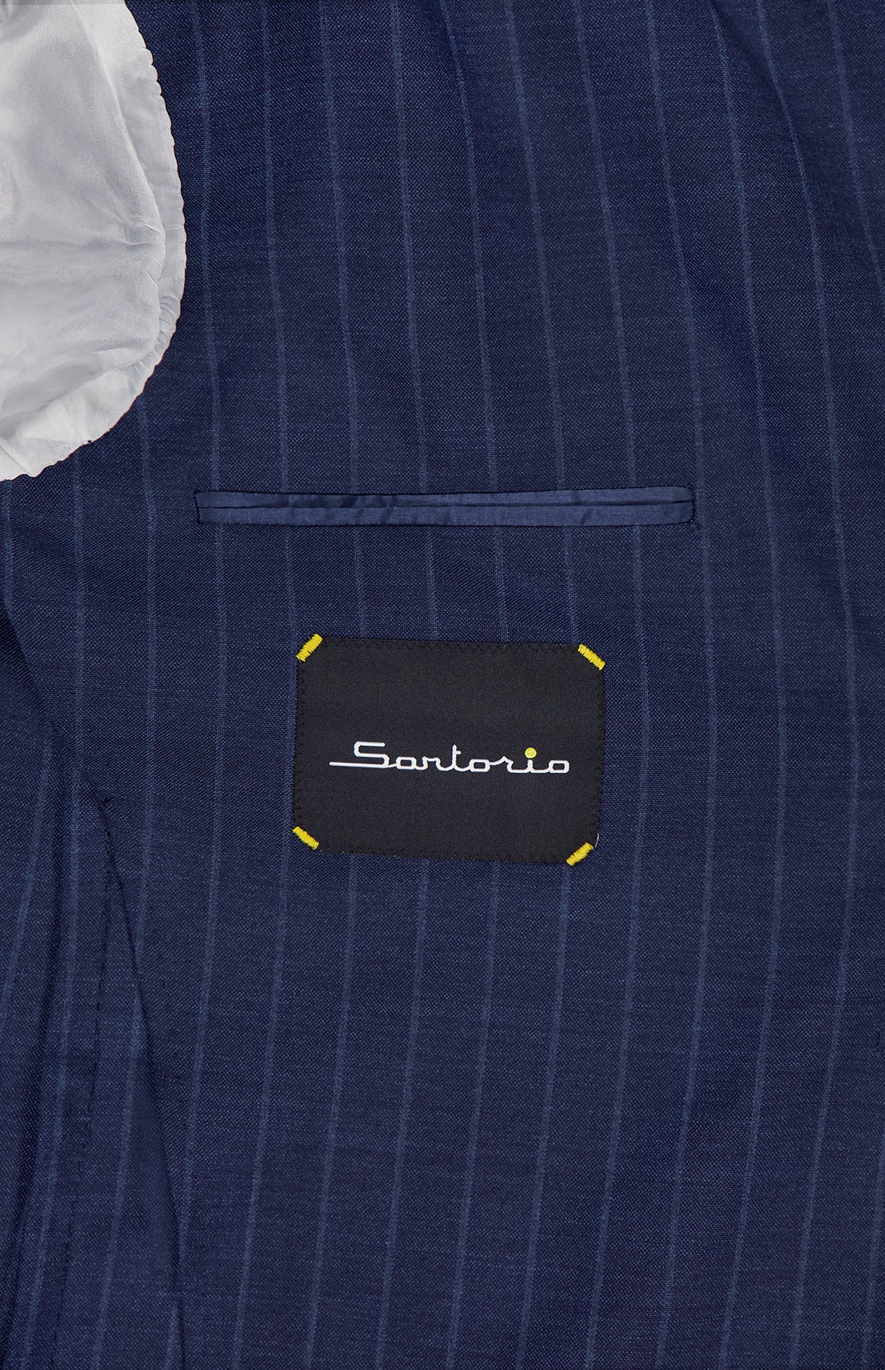 Close-up of the inside of a navy Pinstripe Wool Suit by SARTORIO, featuring white lining and a black "SARTORIO" label with yellow stitching, highlighting this elegant Italian-made virgin wool sportcoat.