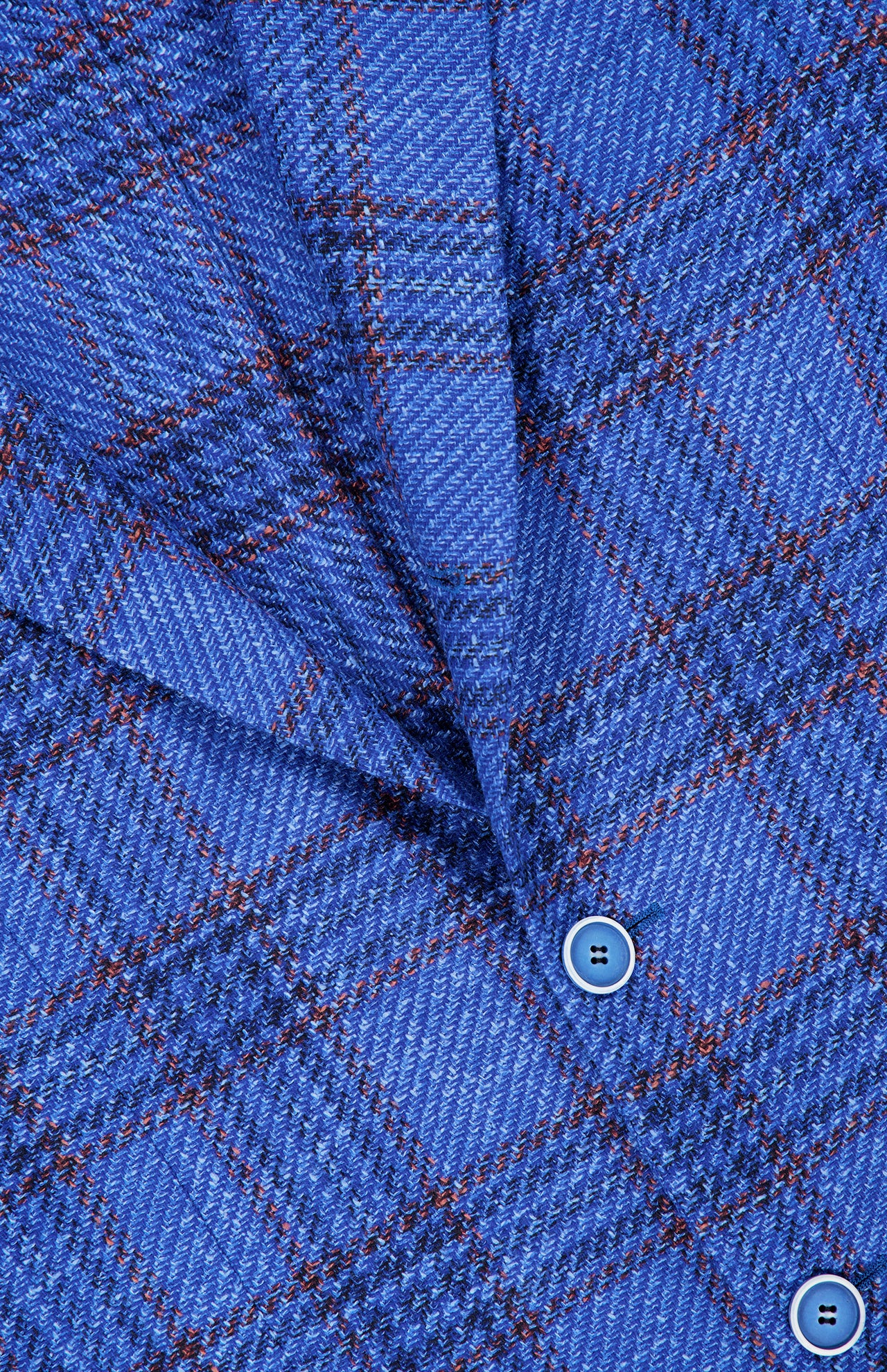 Closeup of the SARTORIO Wool Blend Plaid Sportcoat fabric in blue, showing a diagonal fold and two matching blue buttons. The material displays intersecting darker blue lines and fine orange stripes, highlighting the refined craftsmanship characteristic of this designer sportcoat.