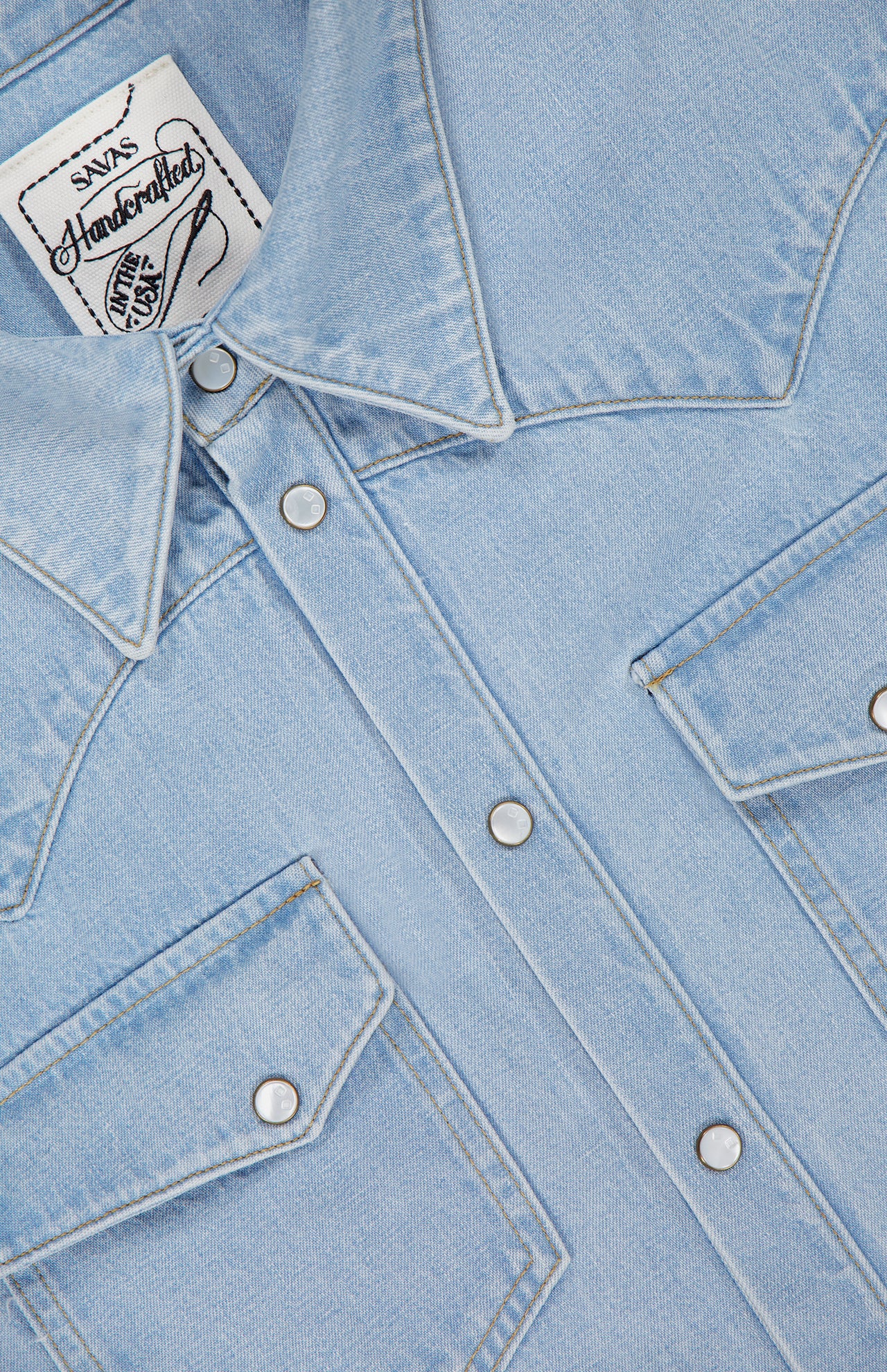 Close-up of a SAVAS Allen Denim Shirt in Japanese selvedge, highlighting snap buttons, two front flap pockets, and a white collar label with text.
