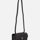 The Symmetry 19 Bag by Savette is a sleek black leather crossbody featuring a long, wide strap and a sophisticated silver oval turnlock closure on the front flap, displayed against a plain white background.