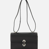 The Symmetry 19 Bag by Savette is a black, rectangular Italian handbag with a silver clasp and double handles, displayed against a plain white background. Its smooth, structured silhouette and minimal detailing exude timeless elegance.