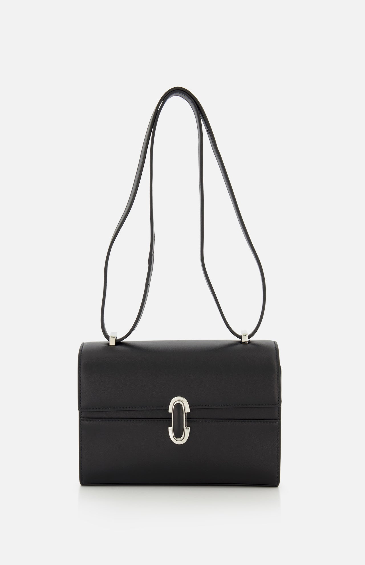 The Symmetry 19 Bag by Savette is a black, rectangular Italian handbag with a silver clasp and double handles, displayed against a plain white background. Its smooth, structured silhouette and minimal detailing exude timeless elegance.