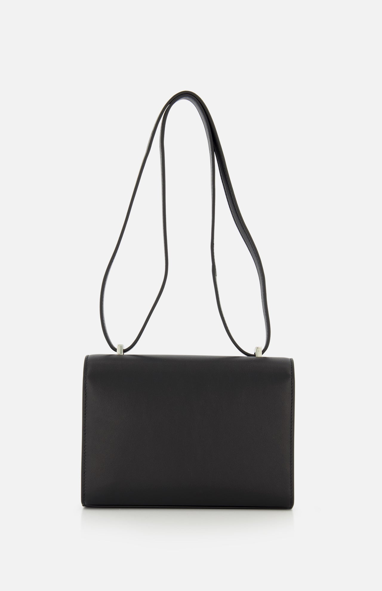 The Symmetry 19 Bag by Savette is a rectangular black leather crossbody featuring a long, slender double strap and an elegant turnlock closure, shown against a plain white background.